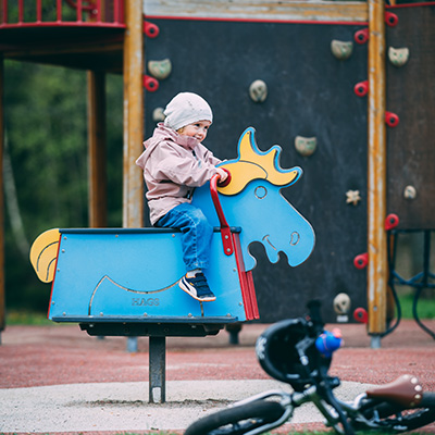 A young child rocks on a horse shaped blue rocker in a playground.